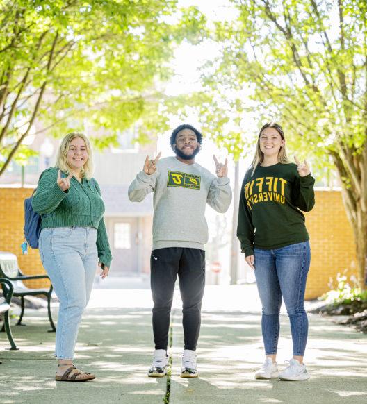 Three smiling students hold up a dragon sign